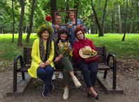 Pięć kobiet w parku, trzy siedza na ławce a dwie stoją za nimi.