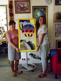 Dwie kobiety stojąc trzymają razem obraz